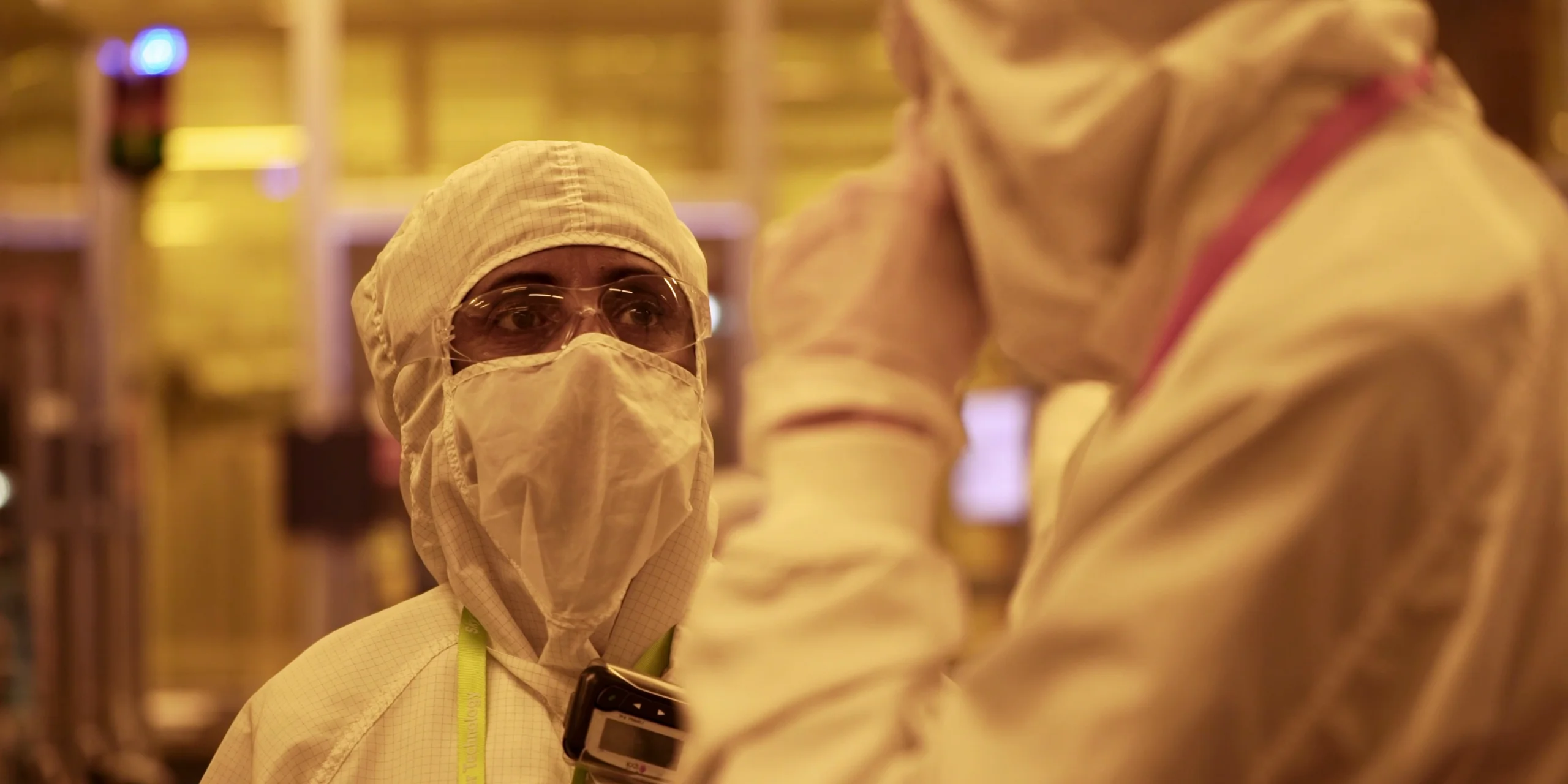 Technicians in cleanroom suits discuss semiconductor manufacturing processes at SkyWater Technology.