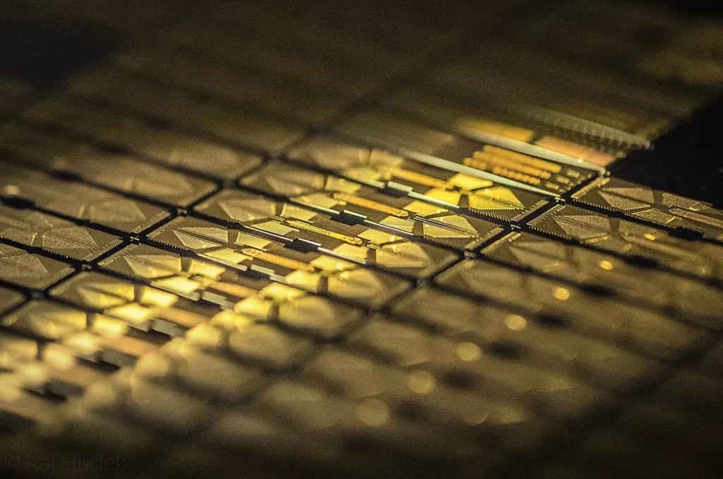 Close-up of a semiconductor wafer with gold-colored circuitry, reflecting light, related to quantum computing technology.