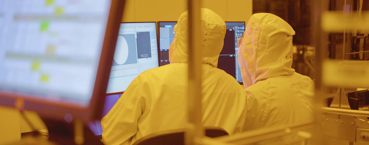 Workers in cleanroom suits operate computer monitors at SkyWater Technology's Austin semiconductor fab.