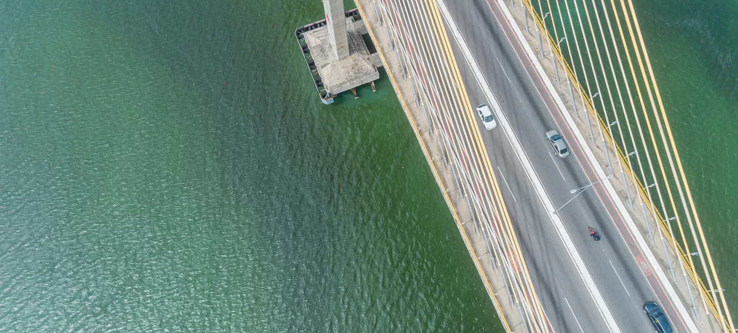 Aerial view of a bridge over a body of water with a few vehicles, including a car and a motorcycle, traveling on it.
