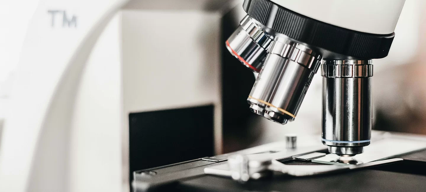Close-up of a microscope in a laboratory setting, highlighting its lenses and stage, symbolizing biomedical research and technology.
