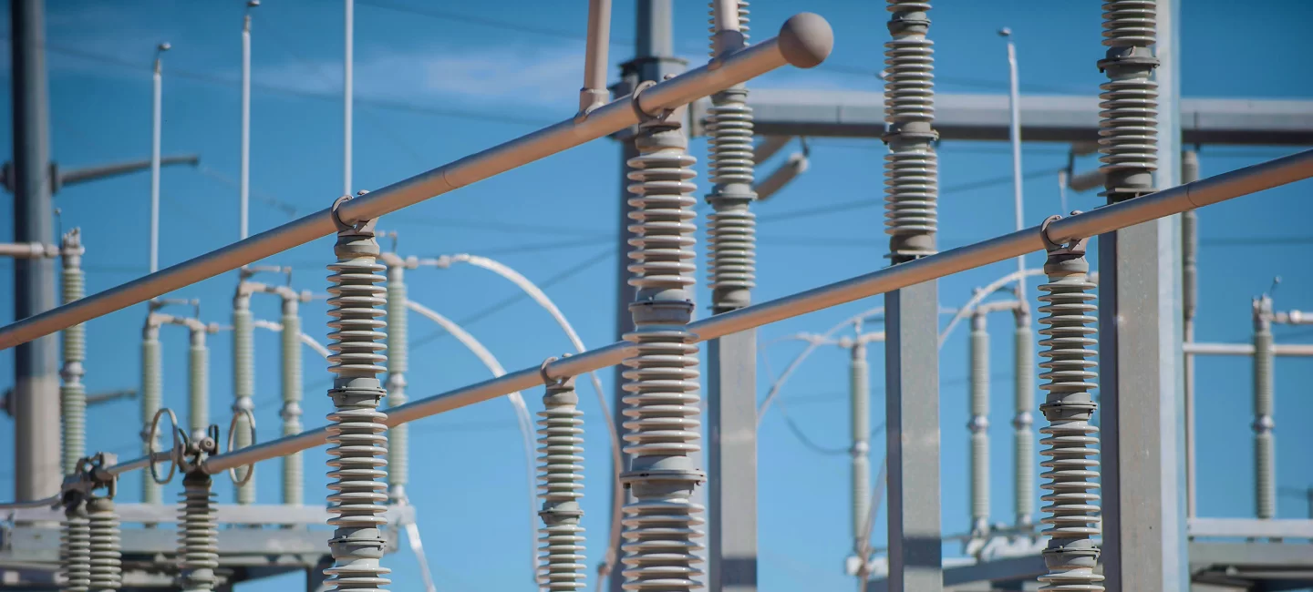 Electrical power grid infrastructure with metal structures and insulators against a blue sky.
