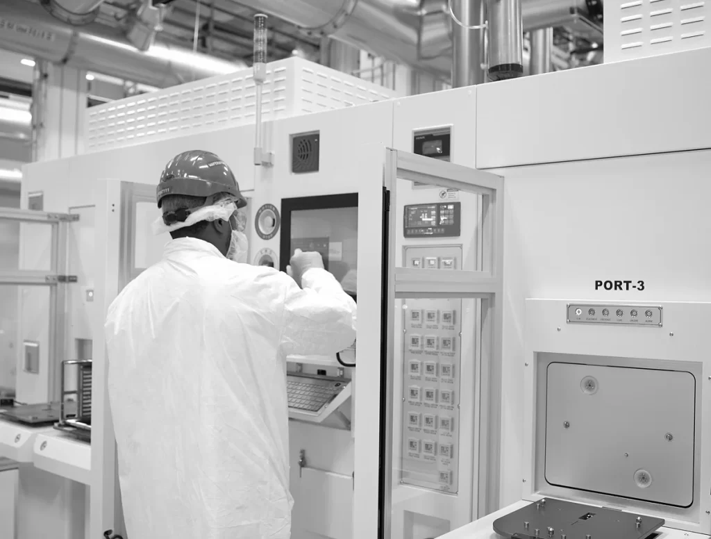 Technician in protective gear operating semiconductor manufacturing equipment in a Florida facility.