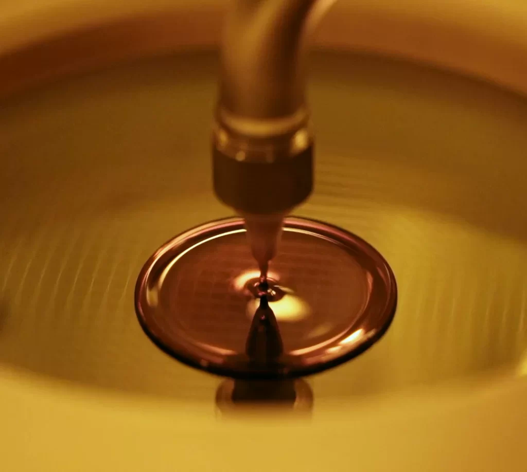 Silicon wafer being processed with a precision tool, reflecting warm lighting, relevant to semiconductor manufacturing.