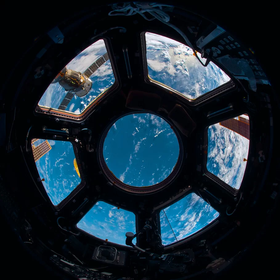 View of Earth from a space station window, showcasing the planet's curvature and cloud formations against a deep blue sky.