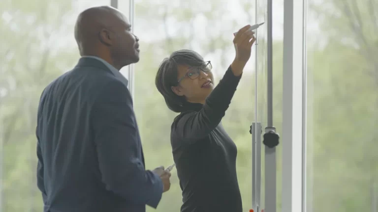 Two professionals collaborate at a whiteboard in a bright office setting, discussing semiconductor technology solutions.