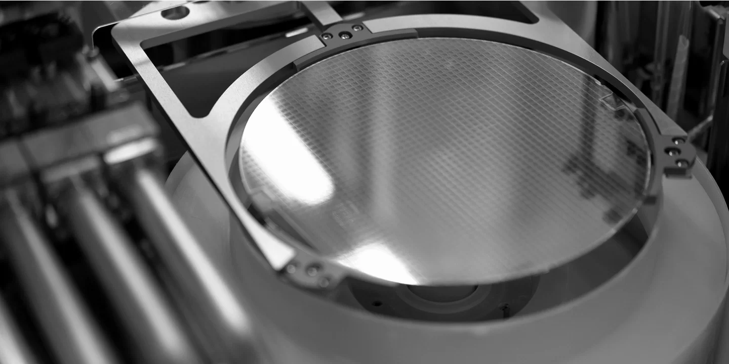 Silicon wafer in a semiconductor manufacturing machine, reflecting light in a black and white setting.